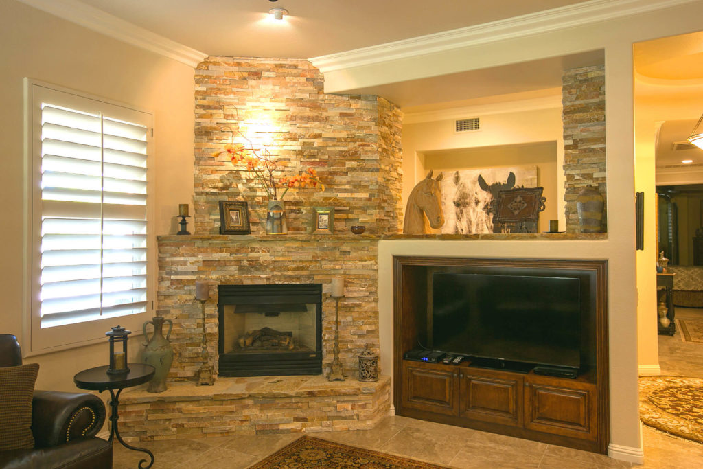 View of a modern living room with crown molding, stone fireplace, and built-in tv niche