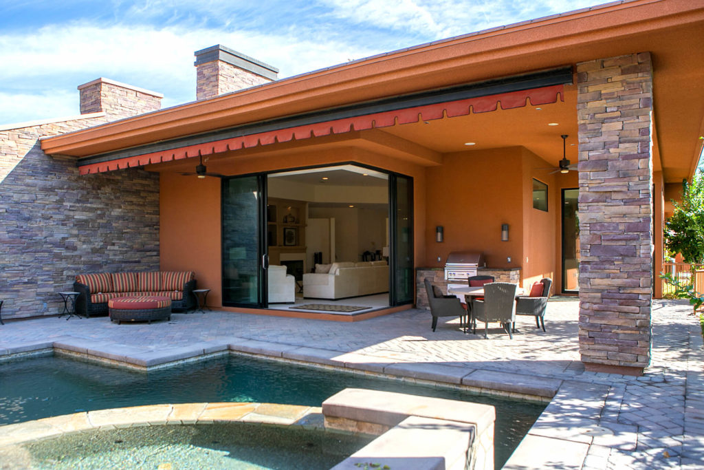 Exterior view of a contemporary home, looking across swimming pool and spa toward stone-tiled patio