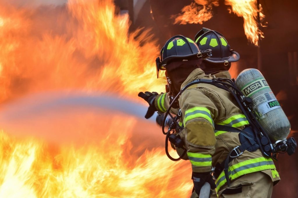 Photo of a pair of firemen as they aim their firehose at a wall of flames