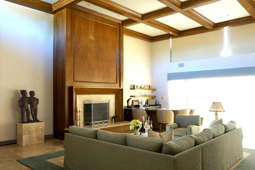 View of a tall room with boxed-beam ceiling and wood-wrapped fireplace