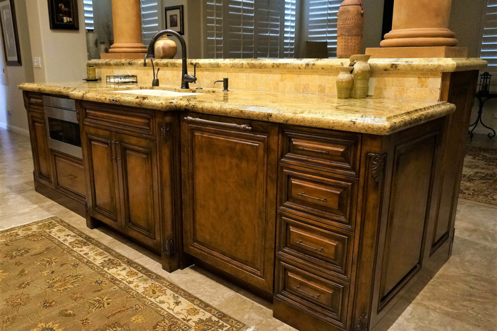 Classic-style custom kitchen cabinets, with raised-panel doors, carved-wood cornerposts, and stone countertops