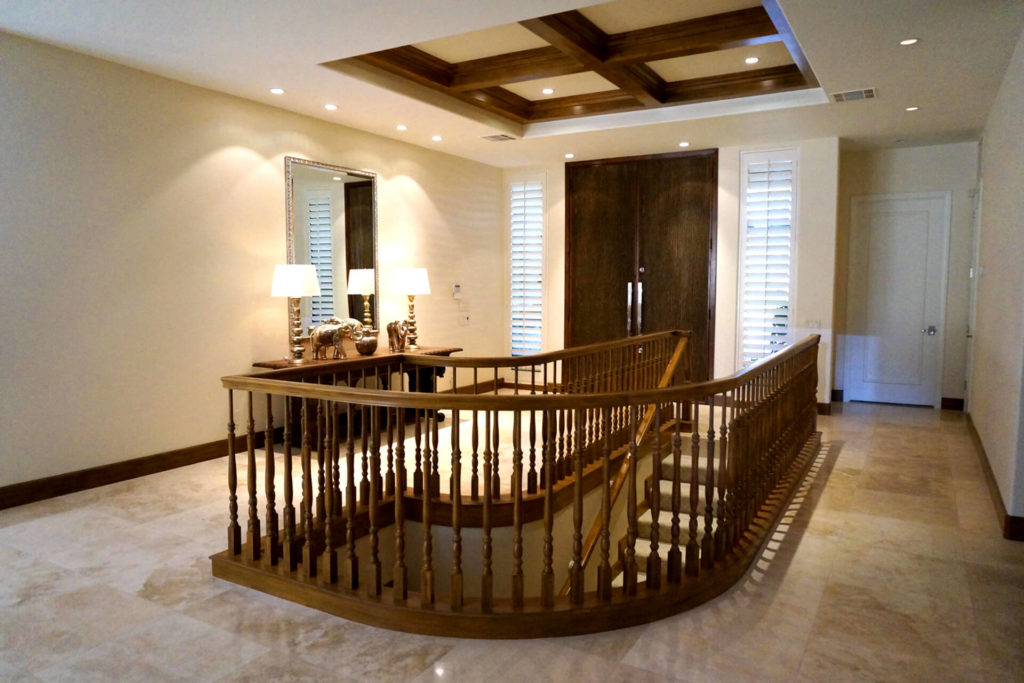 View of the foyer of a contemporary home, with tall, wooden entry door, boxed-beam ceiling, and curved wood stair railings